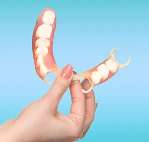 A woman holds flexible dentures in her fingers.
