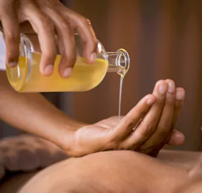 A pale yellow liquid being poured into the other palm during the Sarvangadhara Swedana Ayurveda therapy.
