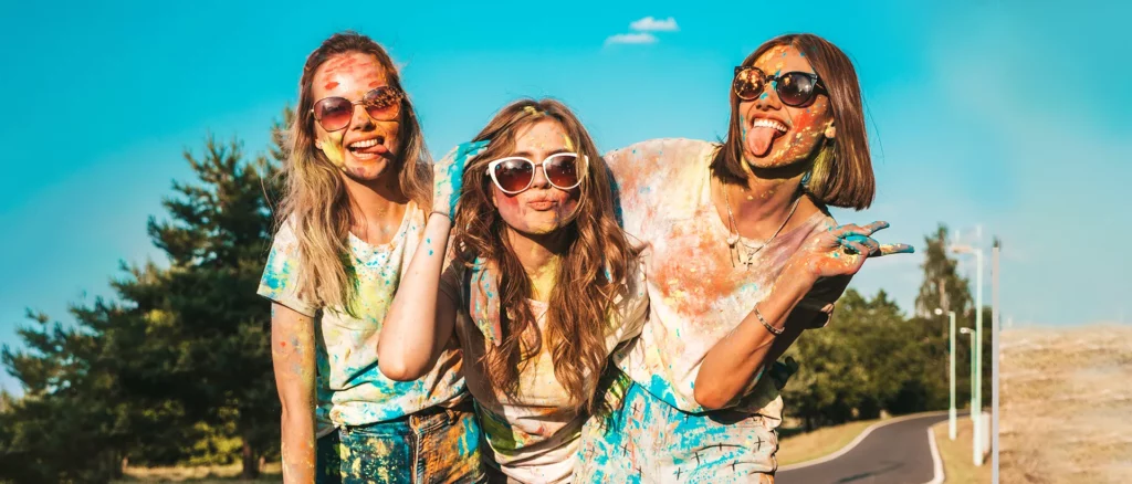 Holi precautions for skin and hair - Three cheerful girls playing Holi without worrying about their hair and skin.