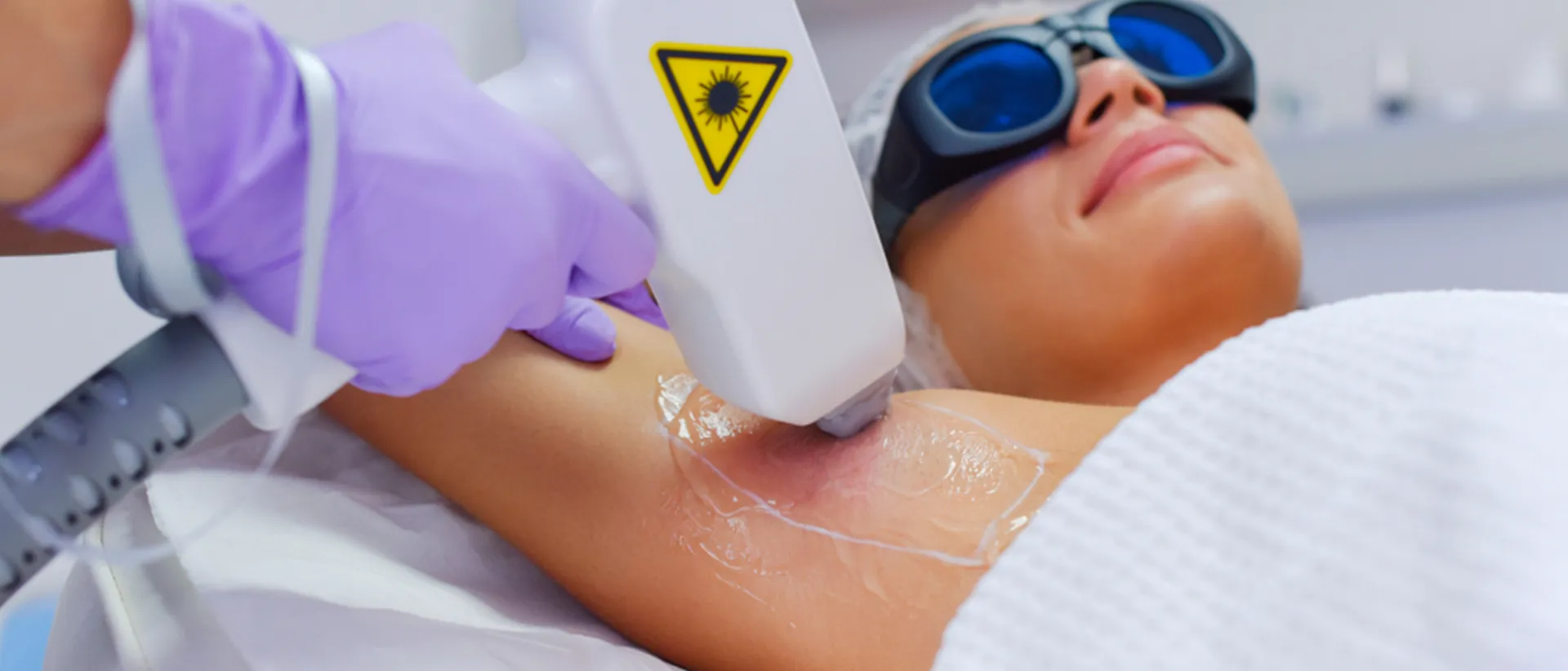 A woman wearing black glasses gets an armpit laser hair removal treatment done.
