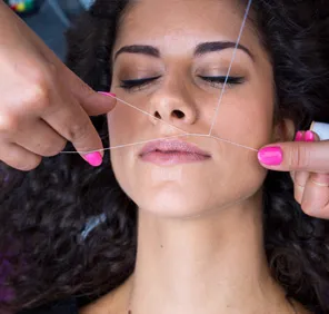 Woman getting threading done at a beauty salon for unwanted facial hair removal.
