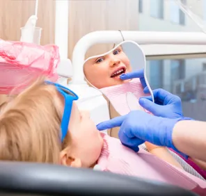 A child looks at the reflection of his teeth in the mirror during early childhood caries treatment.

