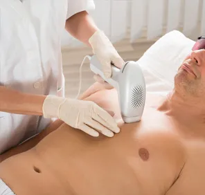 A full body laser hair removal treatment is carried out using a white laser tool pointed at a man's chest.
