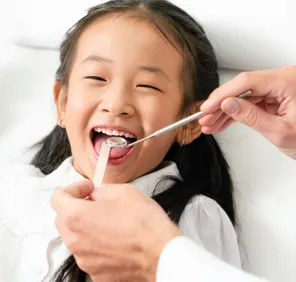 A pediatric dentist in Hyderabad examines a little girl's oral health using metallic dental tools.
