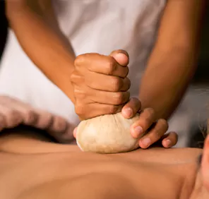 A person uses herbal ingredients during an ayurvedic body massage.
