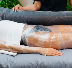 A woman's legs covered with gel and plastic wrap for inch loss treatment.
