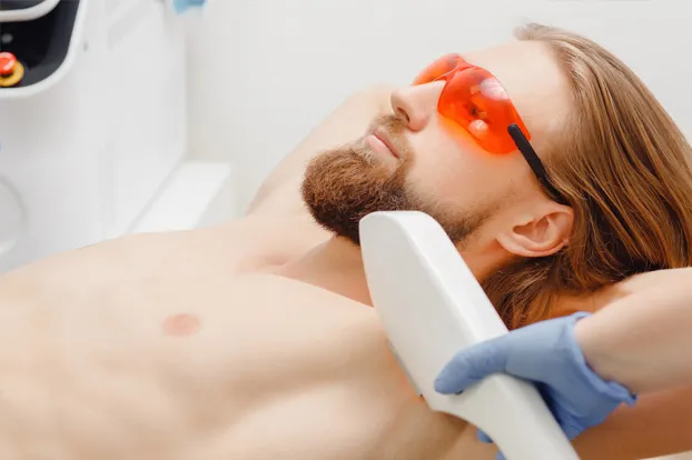 A dermatologist performs armpit laser hair removal on a man wearing orange glasses. 

